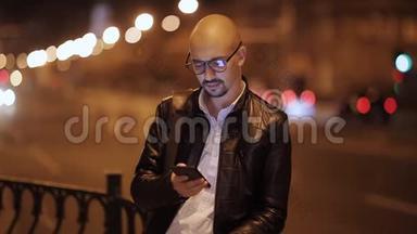 在城市的夜晚，人们使用智能手机上的应用程序短信。 英俊的年轻商人用智能手机微笑快乐